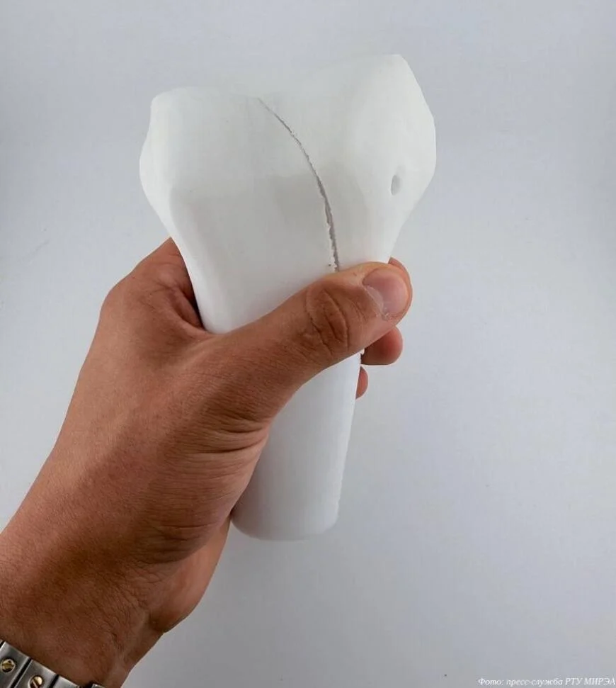 Рука держит белый 3D-печатный имплантат кости с видимым швом